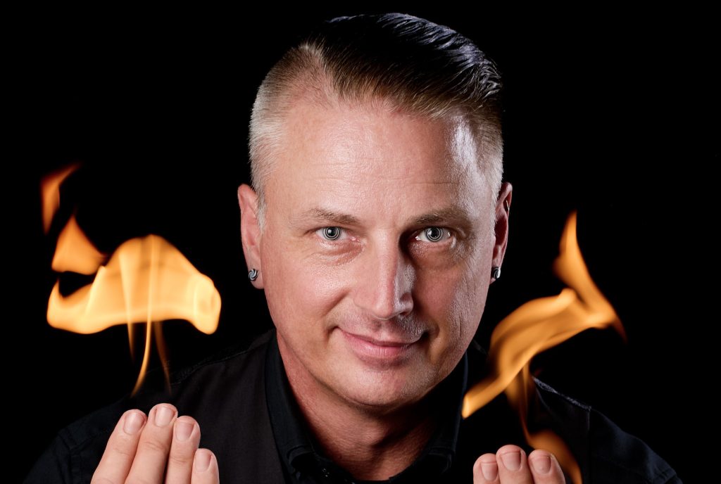 Dr Ace with hypnotic spiral eyes and flames at his fingertips.